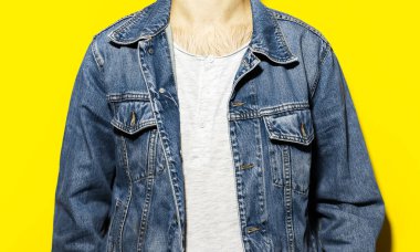 Sarı arka planda kot ceket ve beyaz gömlek giyen genç adamın yakın çekimi..