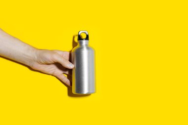 Erkek eliyle yeniden kullanılabilir, su için alüminyum termo şişe tutarken, stüdyo arka planında fotokopi alanı olan sarı renk. Sıfır kayıp. Plastiksiz.