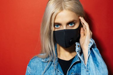 Kırmızı arka planda Coronavirus 'a karşı tıbbi maske takan mavi gözlü sarışın kızın stüdyo portresi..
