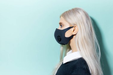 Stüdyo profil portresi, Coronavirus 'a karşı solunum maskesi takan sarışın bir kız. Cyan arkaplan, aqua menthe renk kopyalama alanı.