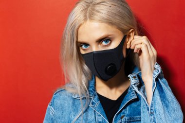 Stüdyo yakın plan portresi mavi gözlü, solunum maskesi takan siyah yüzlü genç bir kız Coronavirus 'a karşı. Kopya alanı ile kırmızı rengin arkaplanı.