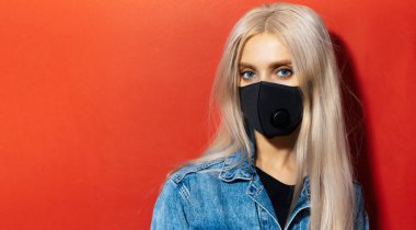 Coronavirus 'a karşı solunum maskesi takan mavi gözlü sarışın kızın stüdyo portresi. Kopya alanı ile kırmızı rengin arkaplanı.