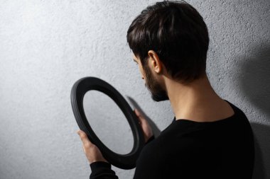 Aynaya bakan genç adamın dramatik portresi. Gri desenli duvarın arkaplanı.