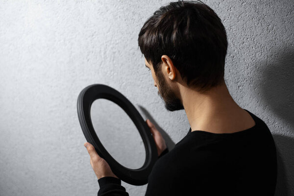 Драматический портрет юноши, смотрящего в зеркало. Фон серой текстурированной стены
.