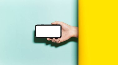 Stüdyonun sarı ve su menisi renklerinin iki stüdyo arkaplanı arasında yatay akıllı telefon tutan erkeklerin yakın çekimi.. 