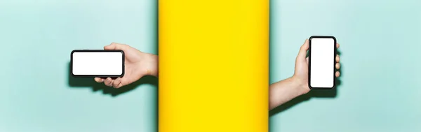 Close-up of male hands holding horizontal and vertical smartphones with mockup between two studio backgrounds of yellow and aqua menthe colors.