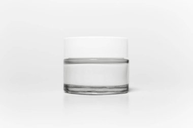 Beyaz stüdyo arka planında izole edilmiş cam kozmetik kavanozuna yakın çekim.