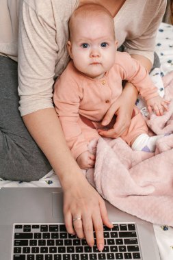 Dizüstü bilgisayarı olan bir anne ve bebek yatakta çalışıyor. Anne karantina sırasında evde çocukla birlikte çalışıyor. Bebek oynarken tanınmayan bir annenin yatakta oturup laptopta çalışmasına yakın plan.