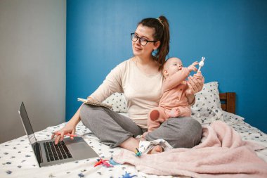 Yatak odasında bebeğin yanında çalışan genç bir anne. Kadın bilgisayarla çalışıyor. Evden çalışıyor.. 