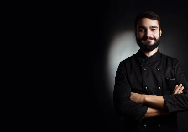 Chef profissional com barba de uniforme preto sobre fundo preto — Fotografia de Stock