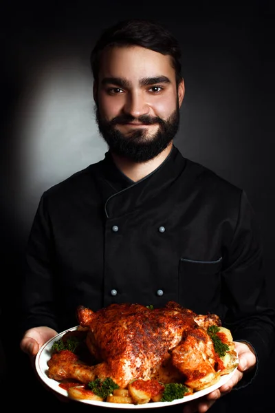 Chef profissional com barba de uniforme preto com frango cozido nas mãos — Fotografia de Stock
