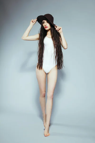 Hermosa chica con el pelo largo en un traje de cuerpo blanco y sombrero —  Fotos de Stock