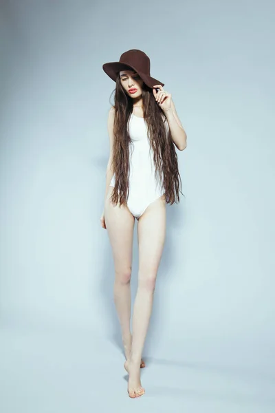Hermosa chica con el pelo largo en un traje de cuerpo blanco y sombrero —  Fotos de Stock