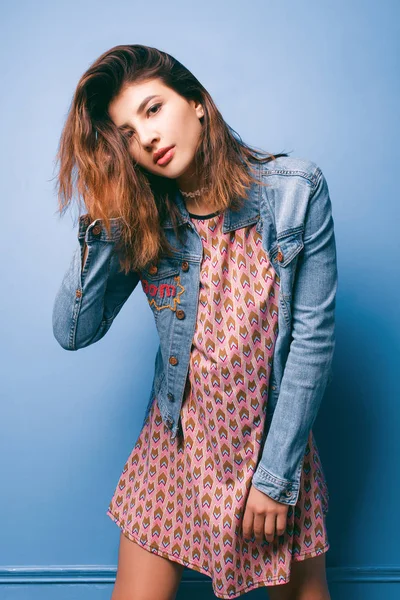 Hermosa chica positiva en una chaqueta vaqueros sobre un fondo azul sonriendo y posando —  Fotos de Stock