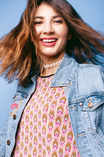 Hermosa chica positiva en una chaqueta vaqueros sobre un fondo azul sonriendo y posando — Foto de Stock