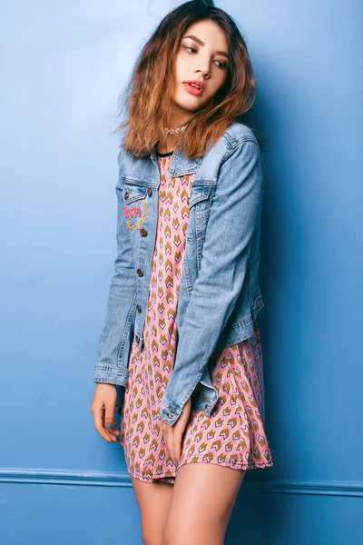 Krásná pozitivní dívka v džínové bundy na modrém podkladu s úsměvem a pózování — Stock fotografie