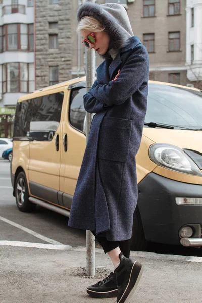 Une fille blonde avec des lunettes et un manteau parcourt les rues de la ville — Photo