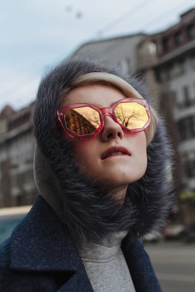Sarışın kız gözlük ve bir kat ile şehrin sokaklarında yürüyor