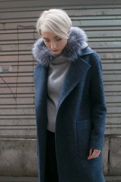 Une fille blonde avec des lunettes et un manteau parcourt les rues de la ville — Photo