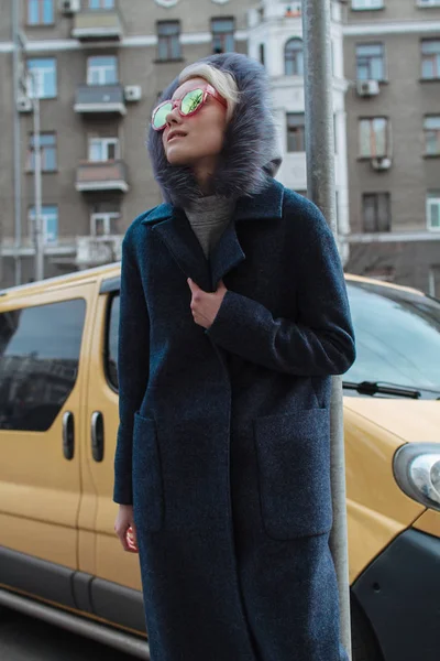 Блондинка в очках и пальто ходит по улицам города — стоковое фото