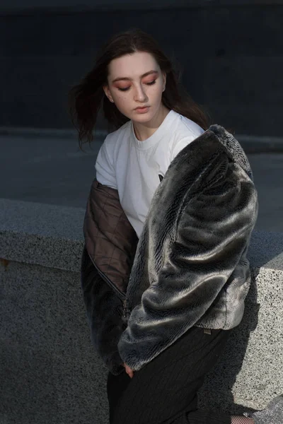 Μια όμορφη και μοντέρνα κοπέλα σε ένα γούνινο παλτό βόλτες στην πόλη, σε μια ηλιόλουστη ημέρα — Φωτογραφία Αρχείου
