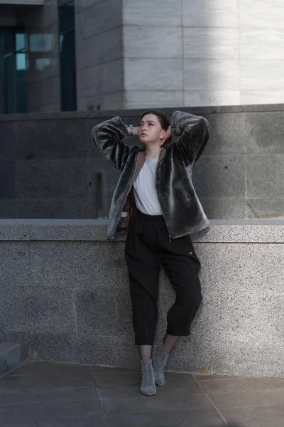 Uma menina bonita e elegante em um casaco de peles caminha na cidade em um dia ensolarado — Fotografia de Stock