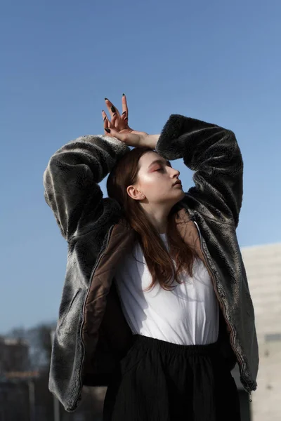 Una chica hermosa y de moda en un abrigo de piel camina en la ciudad en un día soleado — Foto de Stock