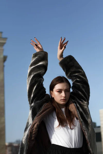 Une belle fille à la mode en manteau de fourrure se promène dans la ville par une journée ensoleillée — Photo