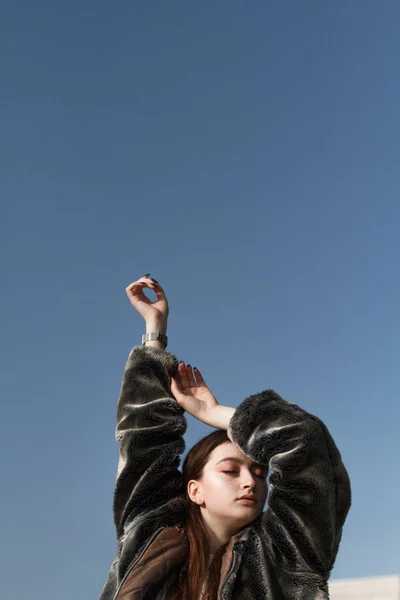 Une belle fille à la mode en manteau de fourrure se promène dans la ville par une journée ensoleillée — Photo