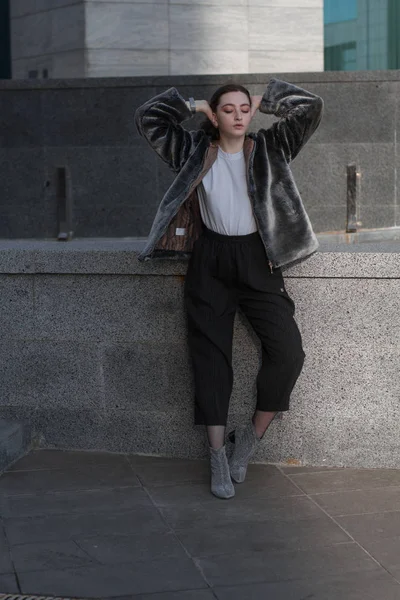 Una chica hermosa y de moda en un abrigo de piel camina en la ciudad en un día soleado — Foto de Stock