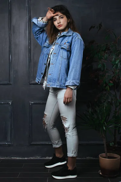 Beautiful girl in jeans poses next to a flower in a pot — Stock Photo, Image