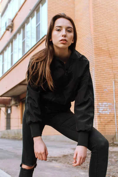 Uma menina jovem e elegante em roupas da moda caminha pela rua na cidade — Fotografia de Stock