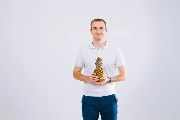 Cheerful and emotional guy holding a pineapple in his hand on a white background — Stock Photo, Image