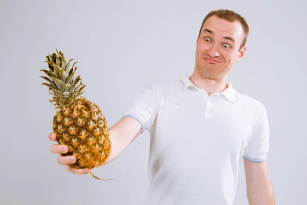 白い背景の上の彼の手でパイナップルを保持している陽気な感情的な男 — ストック写真