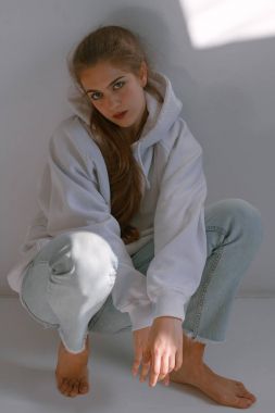 Güzel ve tatlı bir kız kot pantolon ve kazak duruyor beyaz bir duvar