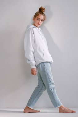 Güzel ve tatlı bir kız kot pantolon ve kazak duruyor beyaz bir duvar