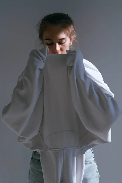 Une belle fille douce en jeans et un sweat-shirt se tient près d'un mur blanc — Photo