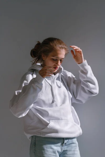 Une belle fille douce en jeans et un sweat-shirt se tient près d'un mur blanc — Photo