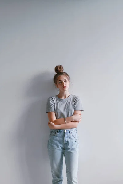 A beautiful, sweet girl in jeans and a sweatshirt stands near a white wall — Stock Photo, Image