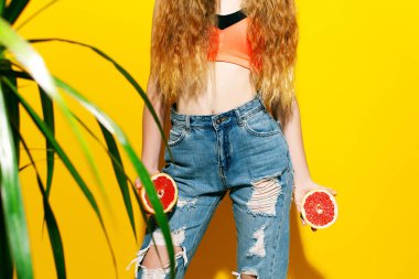 Kız uzun saçlı sarı bir arka plan üzerinde taze greyfurt tutar