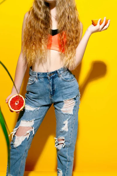 Kız uzun saçlı sarı bir arka plan üzerinde taze greyfurt tutar