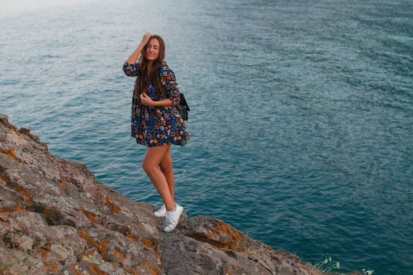 Hermosa chica en un vestido y con un sombrero en las montañas contra el mar — Foto de Stock