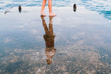 Female wet feet on the pier on the background of the sea