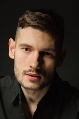 Siyah bir arka plan üzerinde siyah gömlekli adam yakışıklı ve olumlu