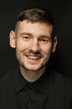 Siyah bir arka plan üzerinde siyah gömlekli adam yakışıklı ve olumlu