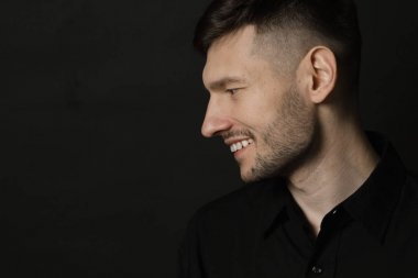 Siyah bir arka plan üzerinde siyah gömlekli adam yakışıklı ve olumlu
