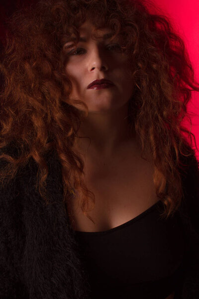 Beautiful red-haired girl with curly hair in the studio on a fabric background