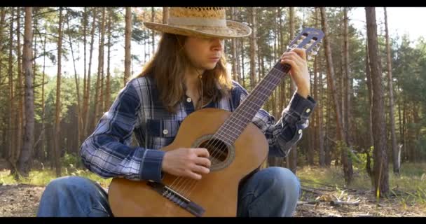 Молодой человек играет на классической гитаре в сосновом лесу — стоковое видео