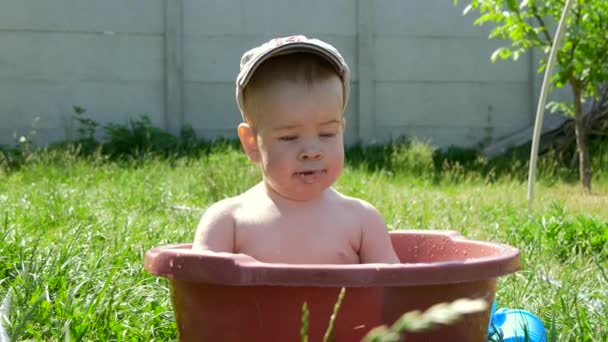 Söt liten pojke ler och spelar i en skål med vatten — Stockvideo