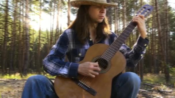 Joven toca la guitarra en el bosque — Vídeo de stock
